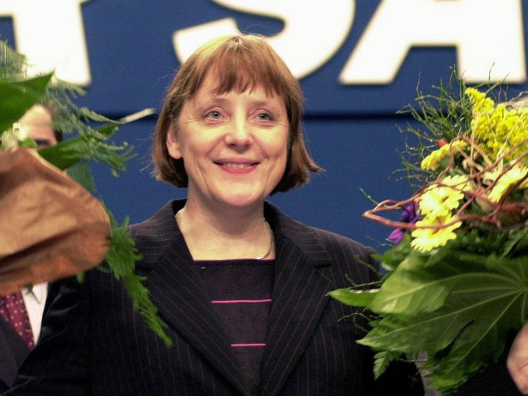 Angela Merkel im Jahr 2000 strahlt mit zwei Blumensträußen in der Hand.