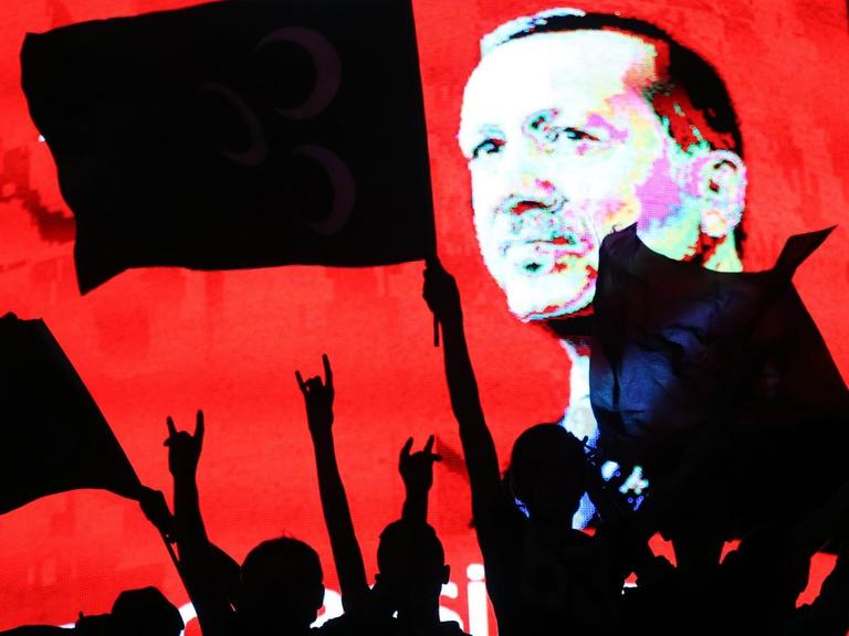 Erdogan-Anhänger mit Fahnen, im Hintergrund Porträt von Erdogan auf einem Bildschirm