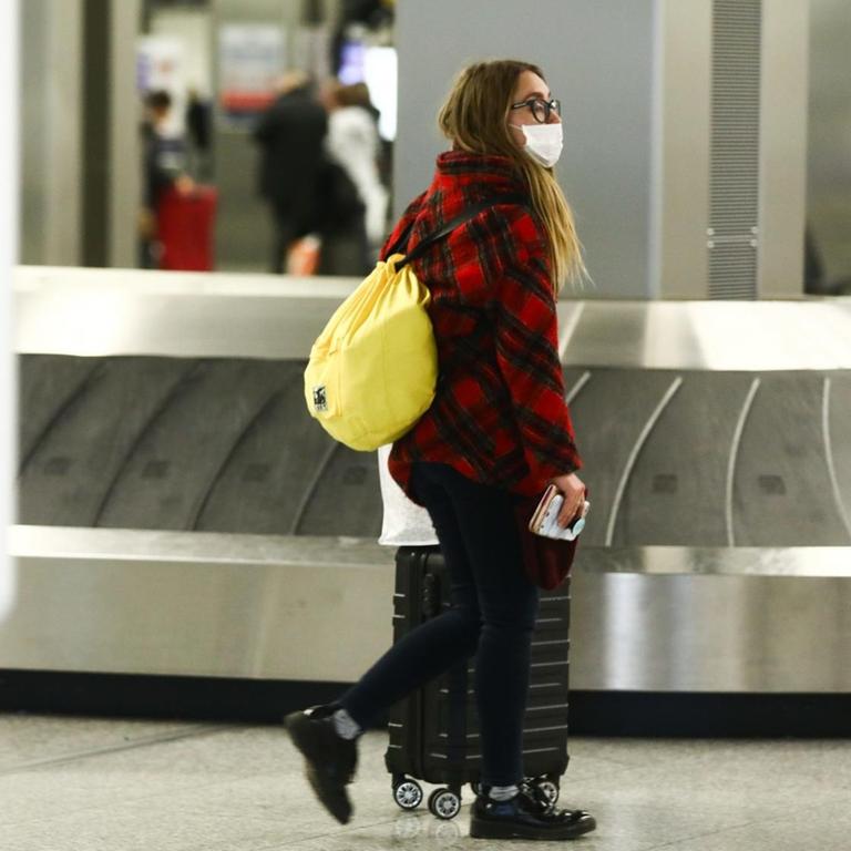 Eine Frau, die gerade in Krakow gelandet ist, schiebt ihren Koffer am Gepäckband vorbei und trägt dabei eine Atemschutzmaske