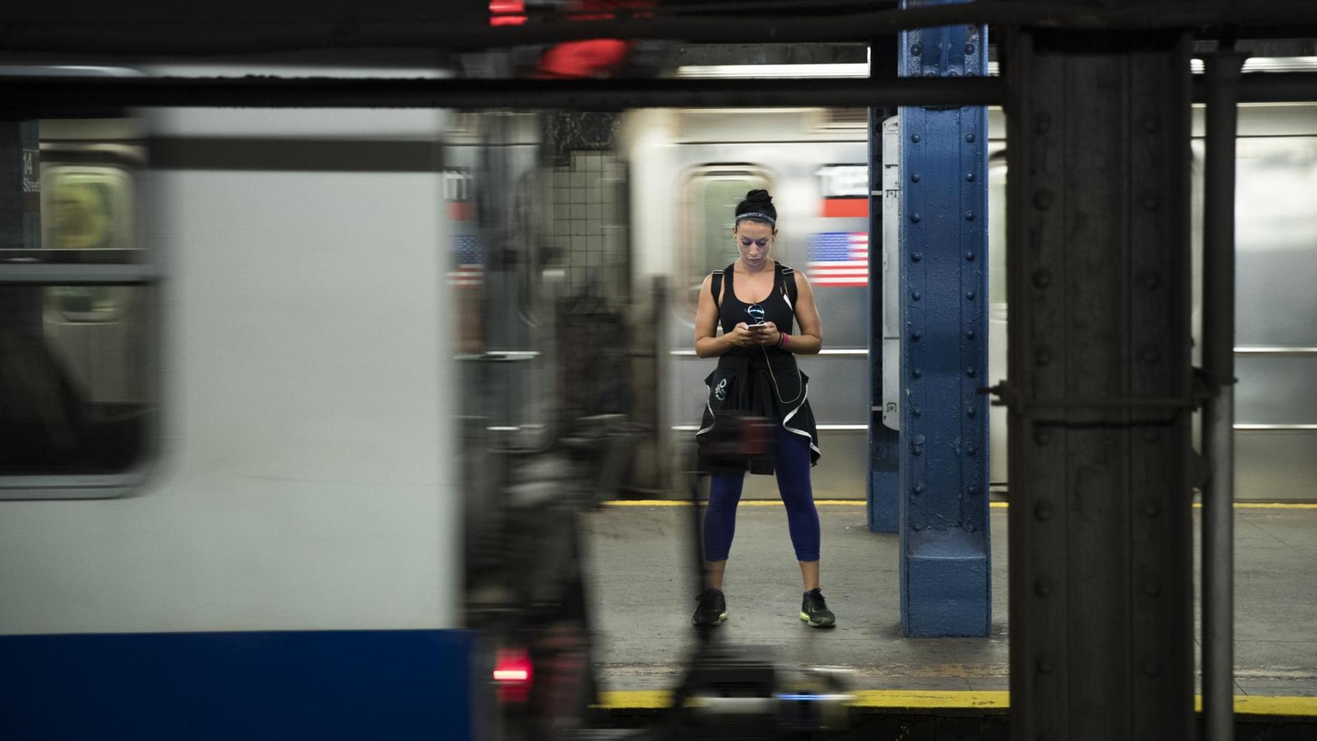 Eine Frau steht breitbeinig in einer U-Bahn, deren Türen geöffnet sind, und schaut auf ihr Handy.