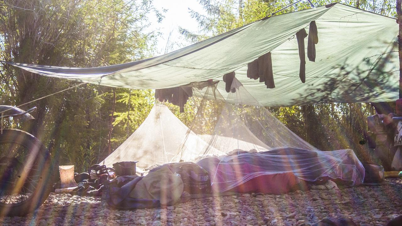 Unter einer großen Zeltplane haben fünf Personen ihr Lager aufgeschlagen. Die Sonne scheint durchs Dach.