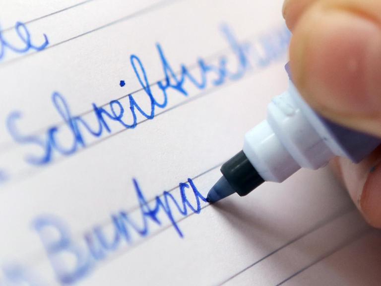 Ein Kind schreibt in Berlin mit verbundener Schreibschrift, der Schulausgangsschrift, in ein Schulheft.