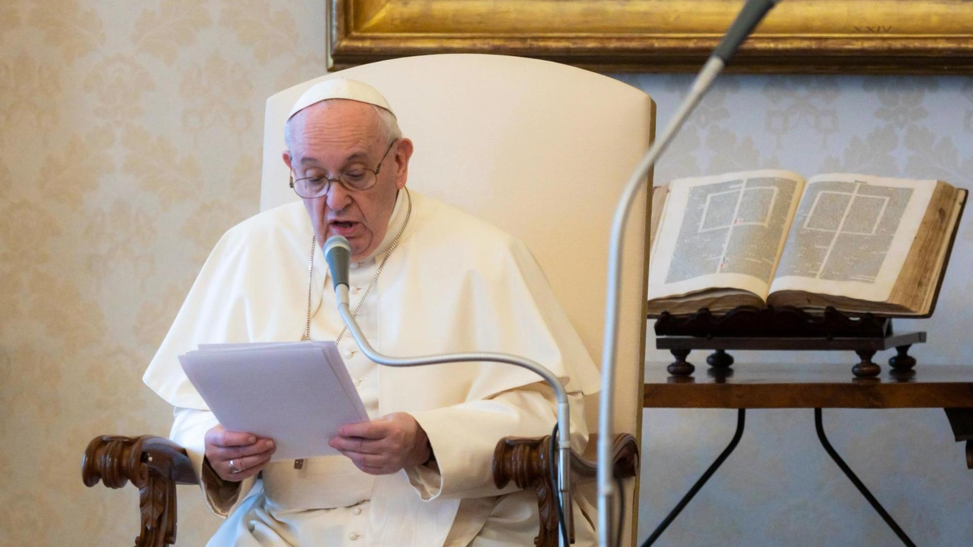 Papst Franziskus sitzt in einem Stuhl und liest etwas vor.