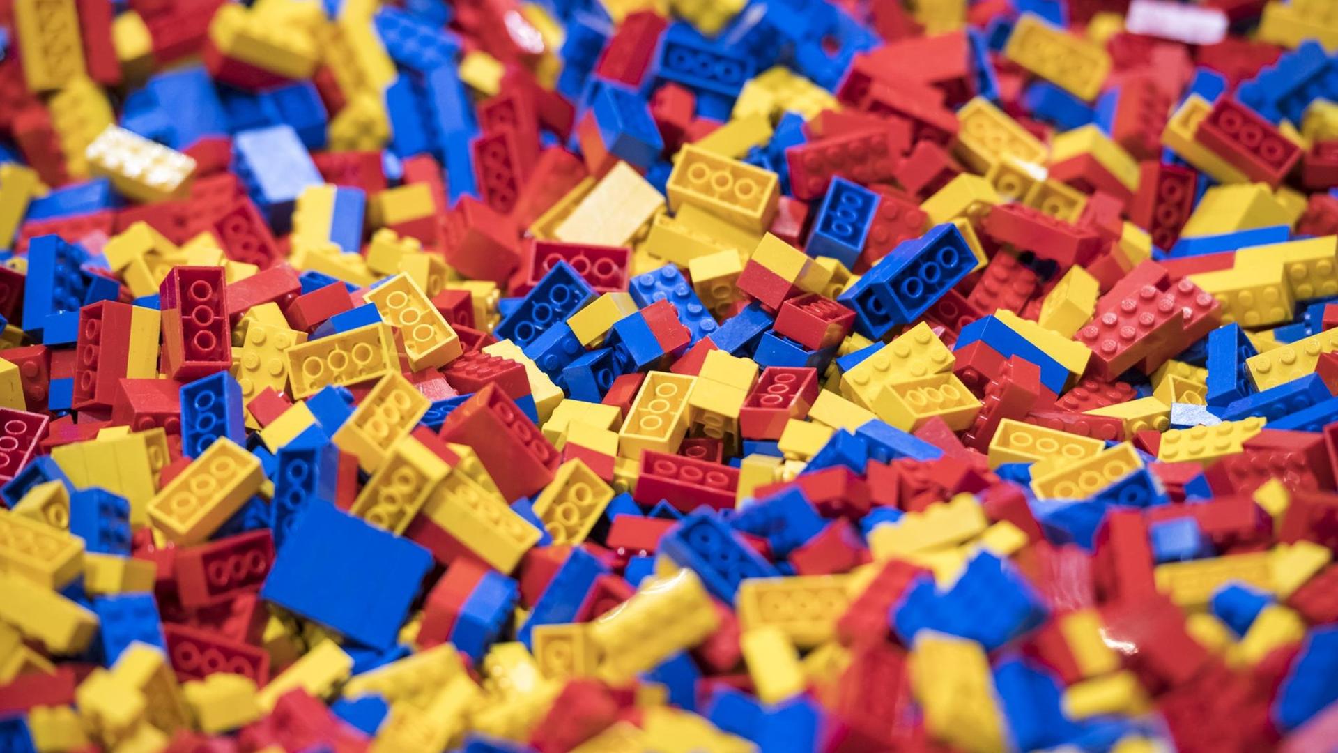 Tausende blaue, rote und gelbe Legosteine liegen durcheinander auf einer Fläche.
