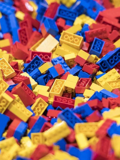 Tausende blaue, rote und gelbe Legosteine liegen durcheinander auf einer Fläche.