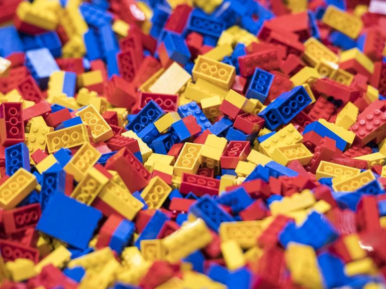 Tausende blaue, rote und gelbe Legosteine liegen durcheinander auf einer Fläche.