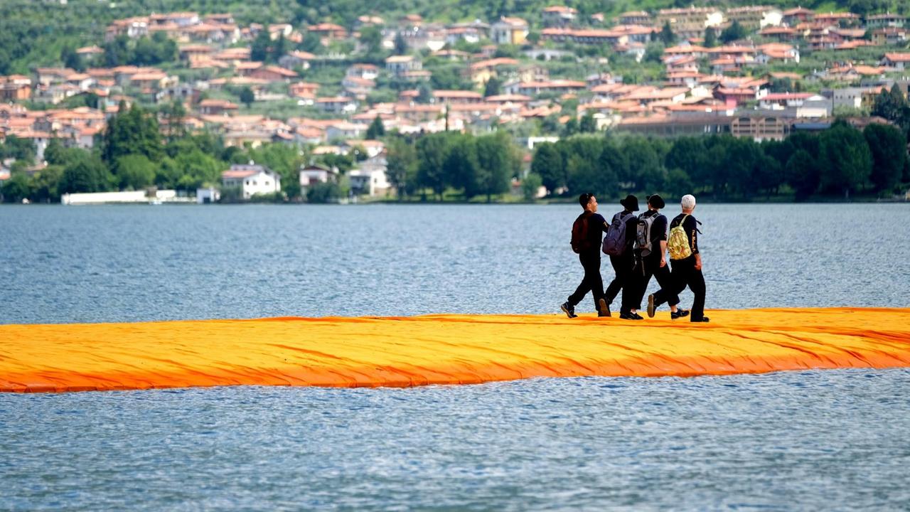 Menschen gehen am 17.06.2016 über orangefarbene, schwimmenden Stege im Rahmen des Projekts "The Floating Piers" von Christo auf dem Lago d'Iseo in Italien. Das Kunstprojekt von Christo auf dem Oberitalienischen See wird am 18.06. eröffnet