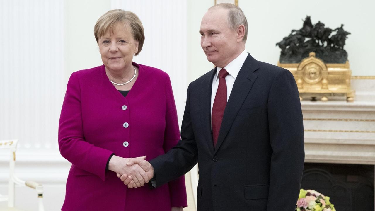 Bundeskanzlerin Merkel und der russische Präsident Putin geben sich die Hand und schauen zu den Fotografen.