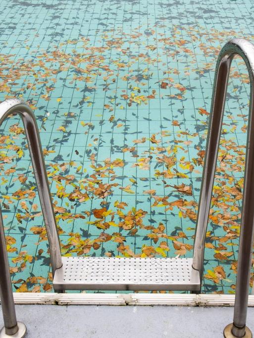 Ein verlassenes Schwimmbecken mit Laub zum Saisonende im Herbst