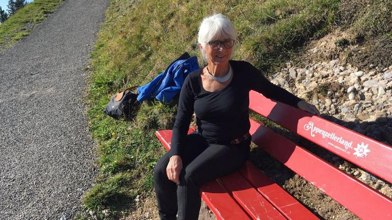 Esther Ferrari sitzt auf einer roten Bank in den Bergen