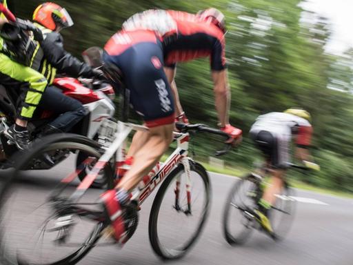 Zwei Radrennfahrer verschwommen von hinten fotografiert, im Hintergrund ein Versorgungsmotorrad.