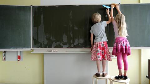 Zwei Grundschülerinnen wischen die Tafel blank.