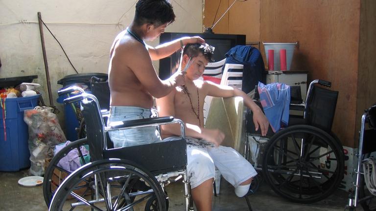 Ein Junge im Rollstuhl schneidet einem zweiten Jungen mit amputiertem Unterschenkel die Haare.
