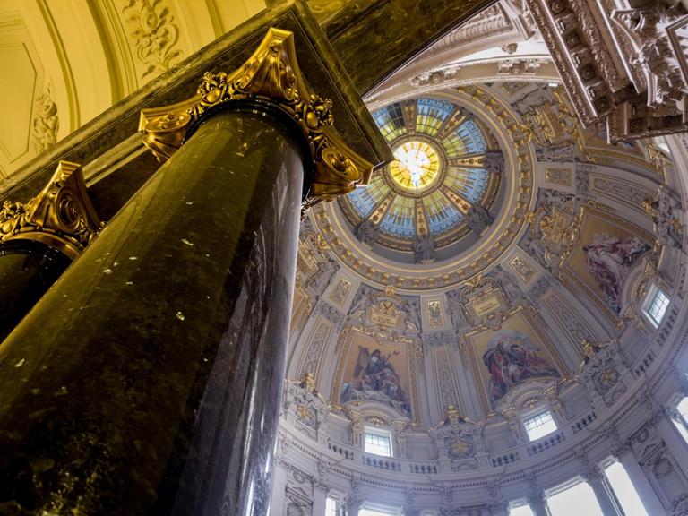 Blick entland einer Säule nach ob in die reich verziehrte Kuppel des Berliner Doms.