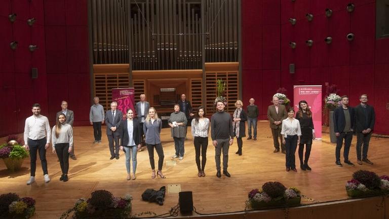 Mehrere Menschen stehen auf einer dekorierten Bühne vor einer großen Orgel und blicken in die Kamera.