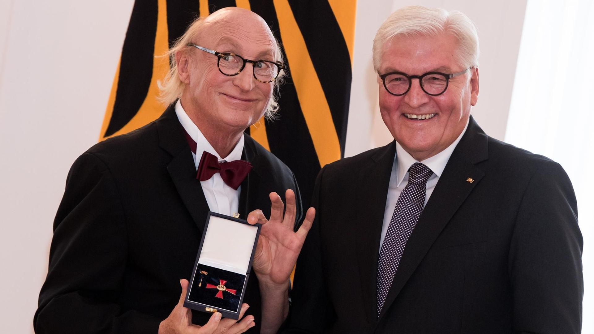 Auf dem Foto ist links der Komiker Otto Waalkes. Er hält den Verdienst-Orden in der Hand. Daneben steht der Bundes-Präsident. Er heißt Frank-Walter Steinmeier.