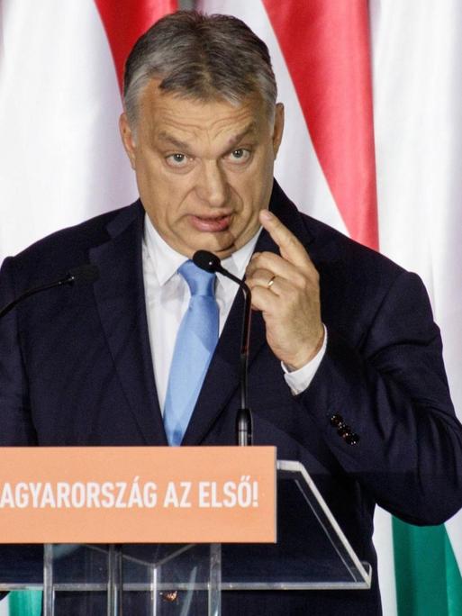 Ungarns Ministerpräsident Viktor Orbán steht bei einer Rede an einem Pult und hebt die linke Hand