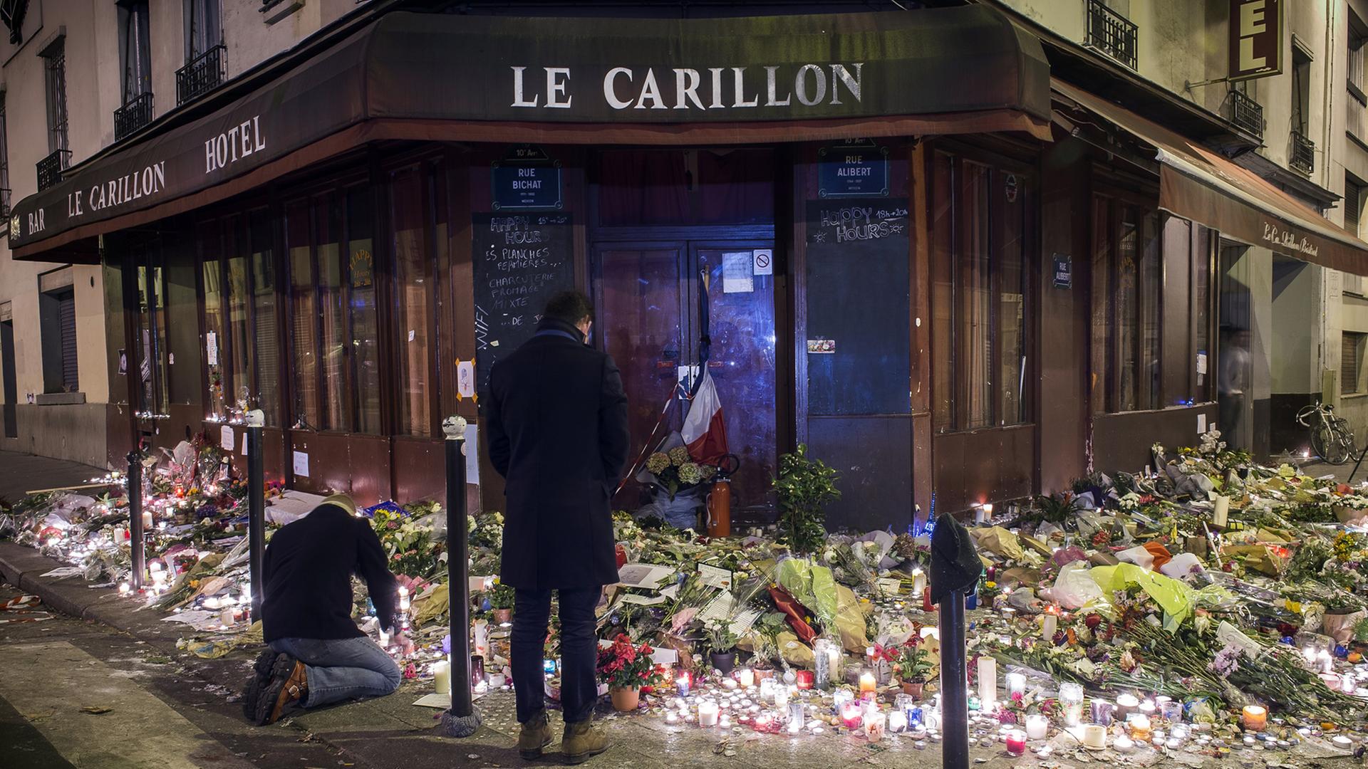 Zwei Männer und Blumen erinnern vor dem Pariser Café Le Carillon an die Attentatsserie.