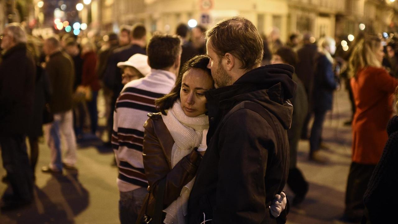 Ein Paar steht am Abend engumschlungen auf der Straße. Um sie herum stehen viele weitere Menschen.