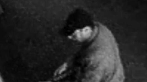 Auf dem schwarz-weißen Überwachungsbild einer Kamera ist ein Mann mit Schirmmütze zu sehen, der ein Gewehr trägt.