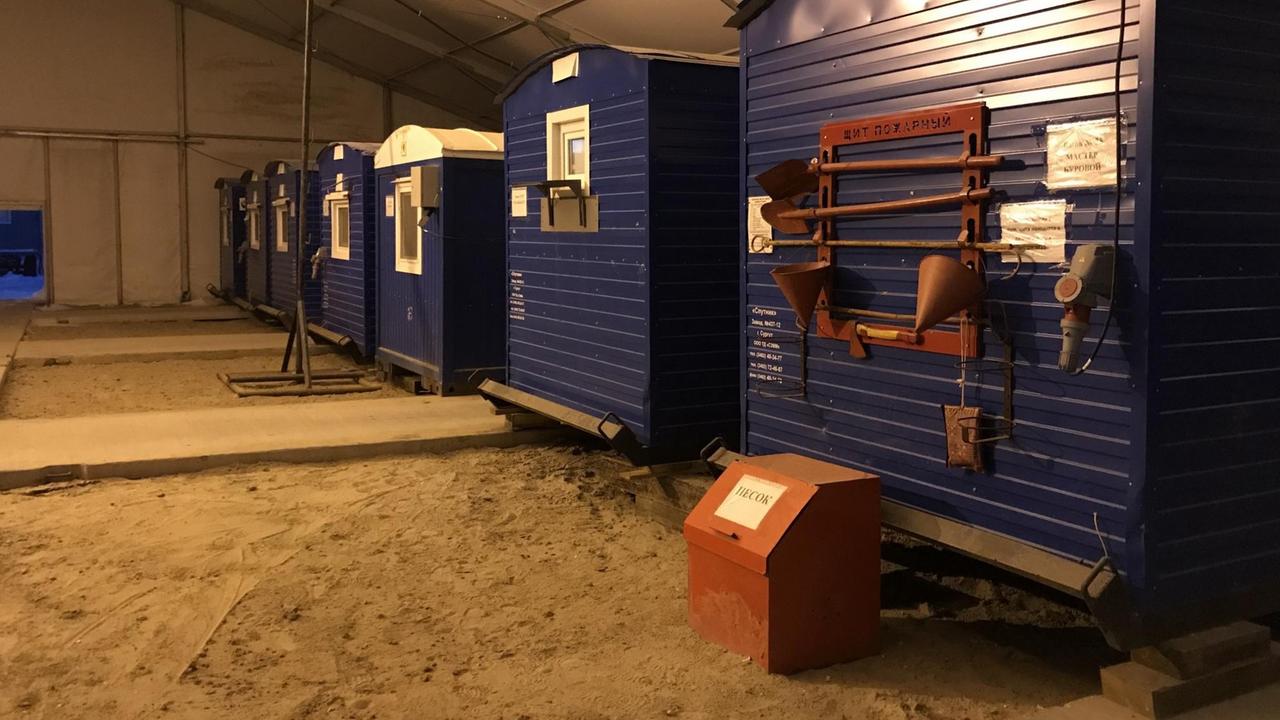 In einer Halle stehen nebeneinander blaue Container, die an Eisenbahnwaggons erinnern