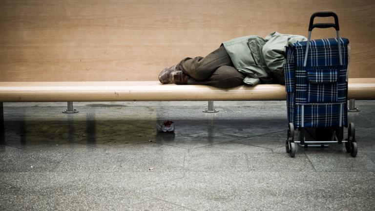 Ein Obdachloser schläft auf einer Parkbank.