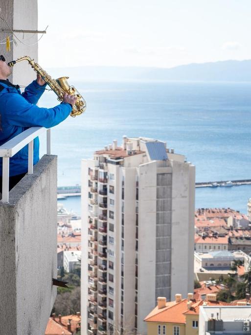 Ein Mann spielt Saxophon auf seinem Balkon und überblickt dabei die Hafenstadt von Rijeka in Kroatien.
