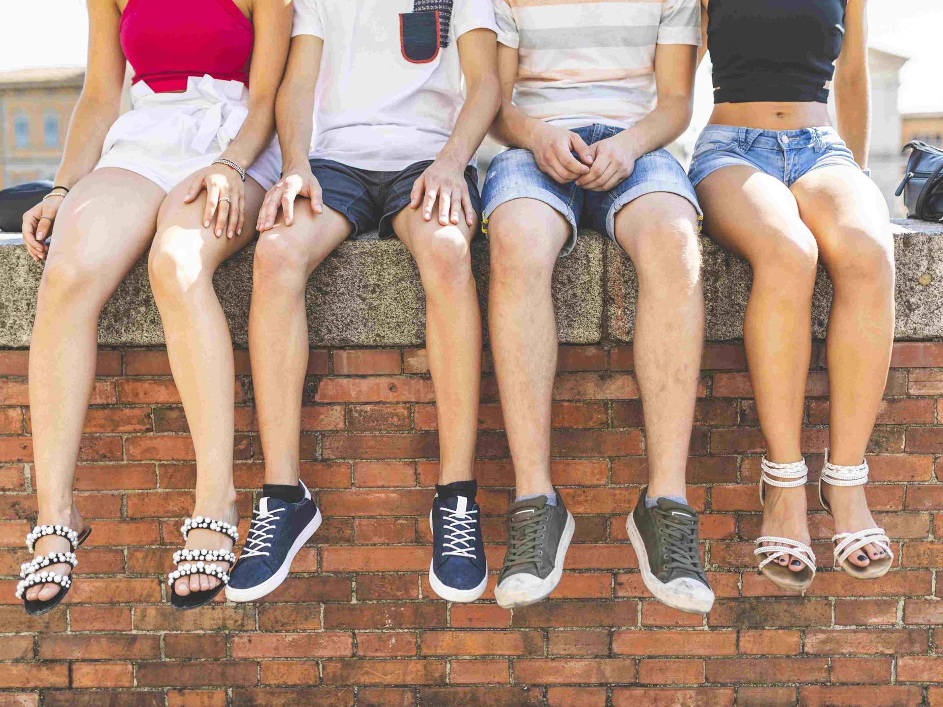 Vier Jugendliche sitzen auf einer Mauer und lassen die Füße baumeln.