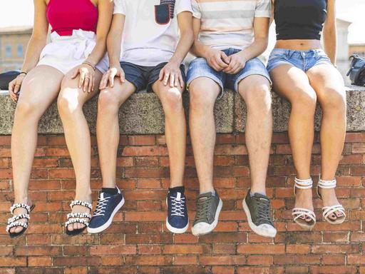 Vier Jugendliche sitzen auf einer Mauer und lassen die Füße baumeln.