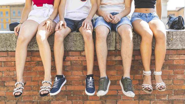 Vier Jugendliche sitzen auf einer Mauer und lassen die Füße baumeln.