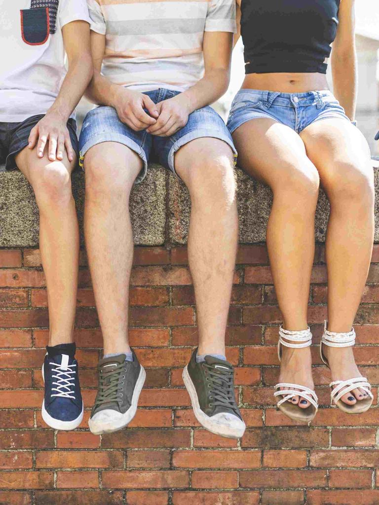 Vier Jugendliche sitzen auf einer Mauer und lassen die Füße baumeln.
