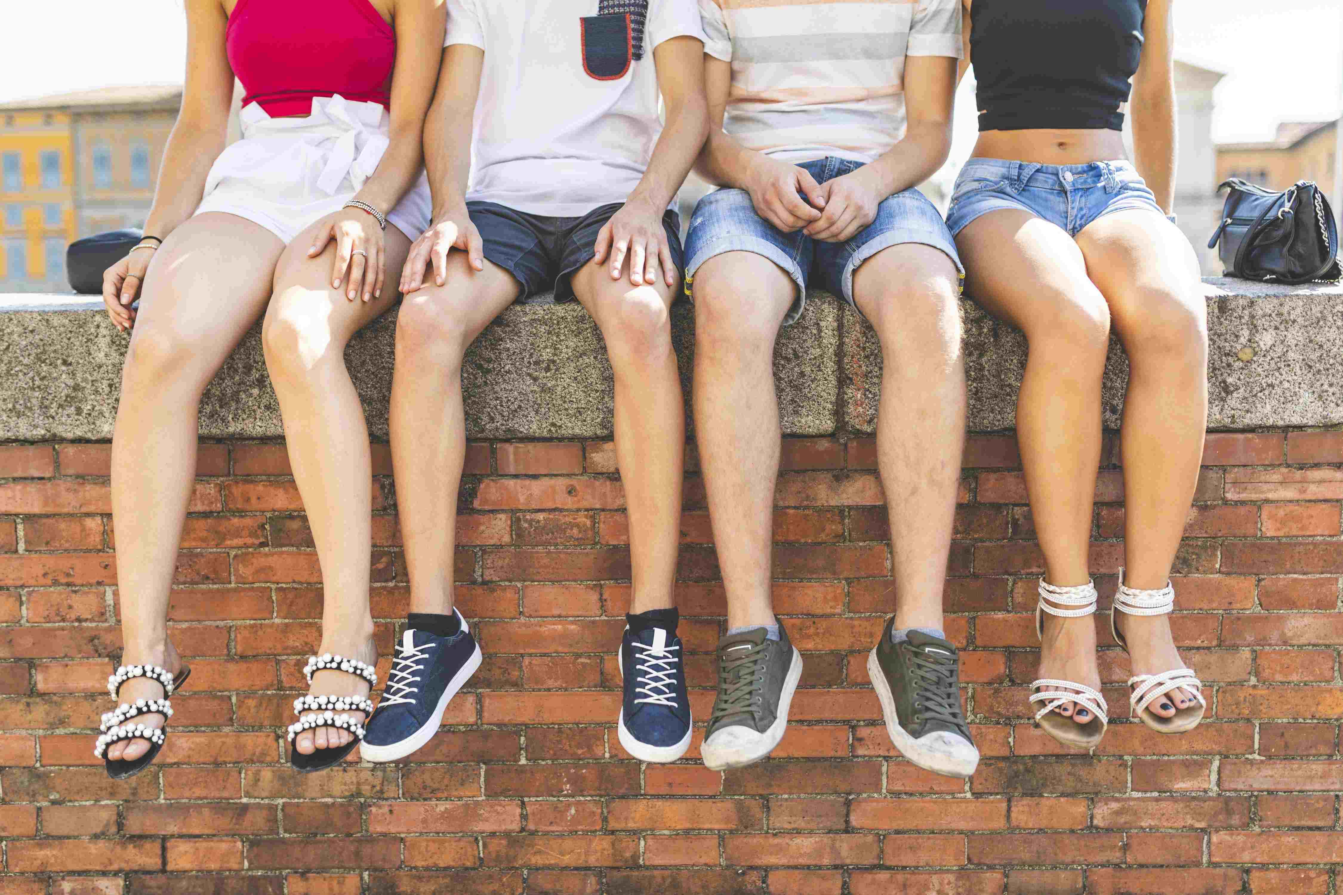 Vier Jugendliche sitzen auf einer Mauer und lassen die Füße baumeln.