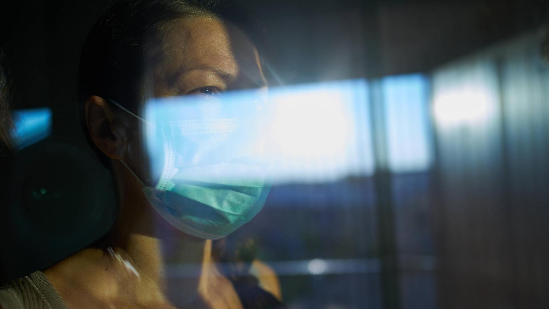 Eine Frau mit Mundschutz schaut durch eine Fensterscheibe