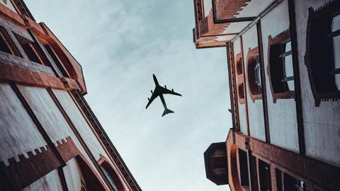 Ein Flugzeug am Himmel zwischen zwei engen Altbau-Fassaden.