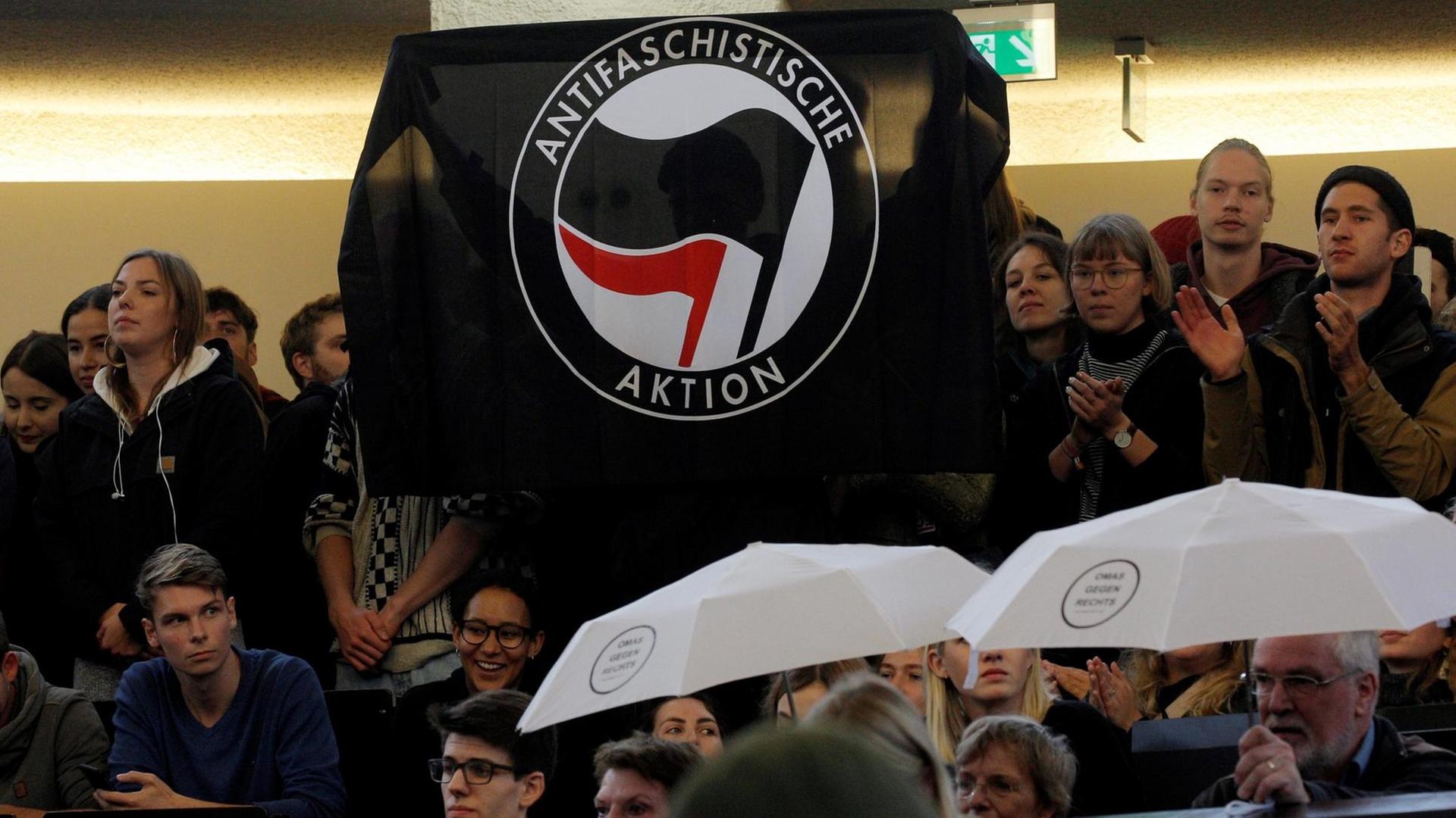 Demonstrierende im Hörsaal halten eine Fahne hoch, auf der steht: Antifaschistische Aktion.