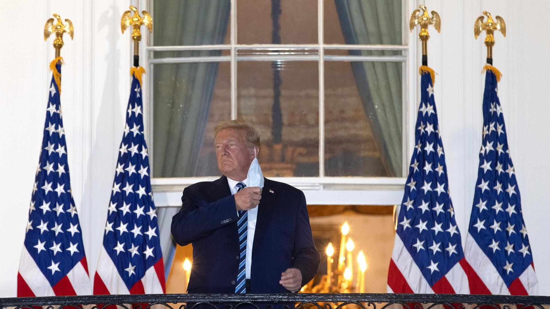 Präsident Trump steht auf dem Balkon am Weißen Haus und nimmt seine Schutzmaske ab