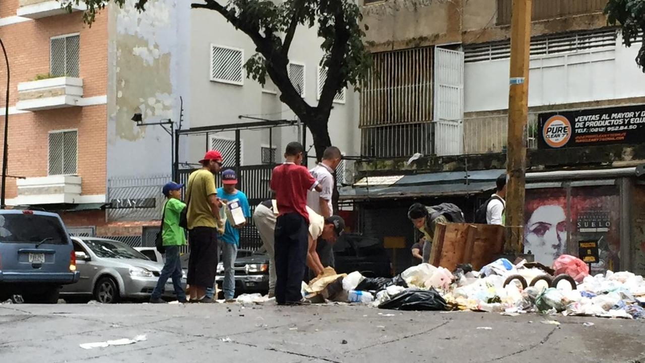 Auf einer Straße in Caracas wühlen junge Männer in Mülltüten.