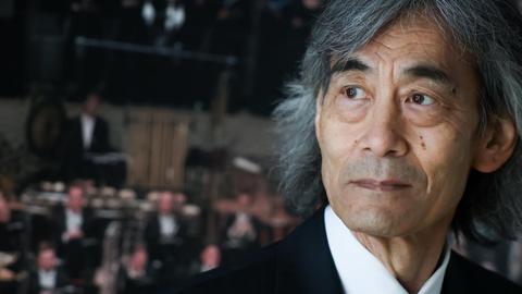 Kent Nagano steht vor einem Poster, das Musiker in den Rängen der Elbphilharmonie zeigt.