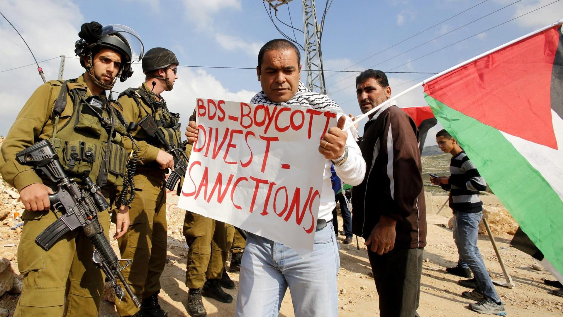 Palästinensische Demonstranten mit Plakate, die sich auf die BDS-Bewegung (Boycott, Divestment and Sanctions) beziehen.