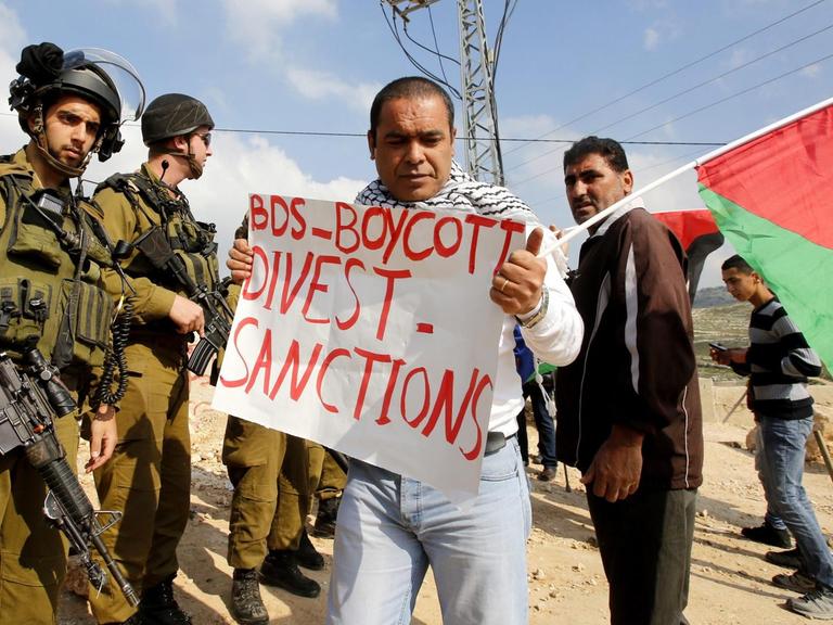 Palästinensische Demonstranten mit Plakate, die sich auf die BDS-Bewegung (Boycott, Divestment and Sanctions) beziehen.