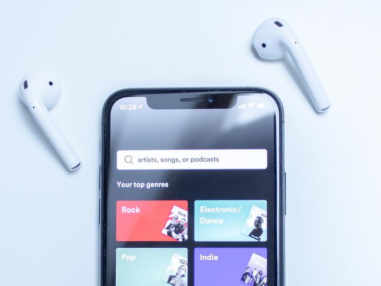 Eine Sachaufnahme zeigt ein Mobiltelefon mit der Spotify-App und moderen Bluetooth-Kopfhörern.