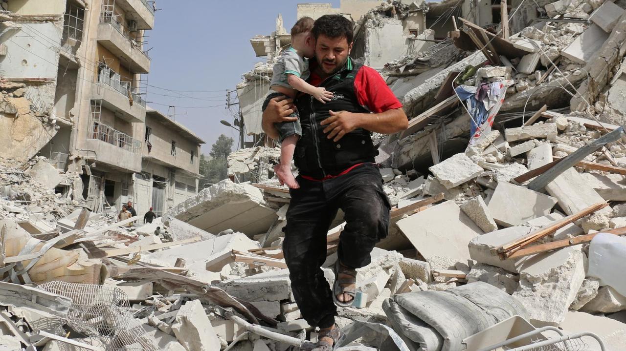 Ein Mann trägt sein Kind in Aleppo am Samstag, 24.09.2016, aus den Trümmern eines zerstörten Gebäudes.