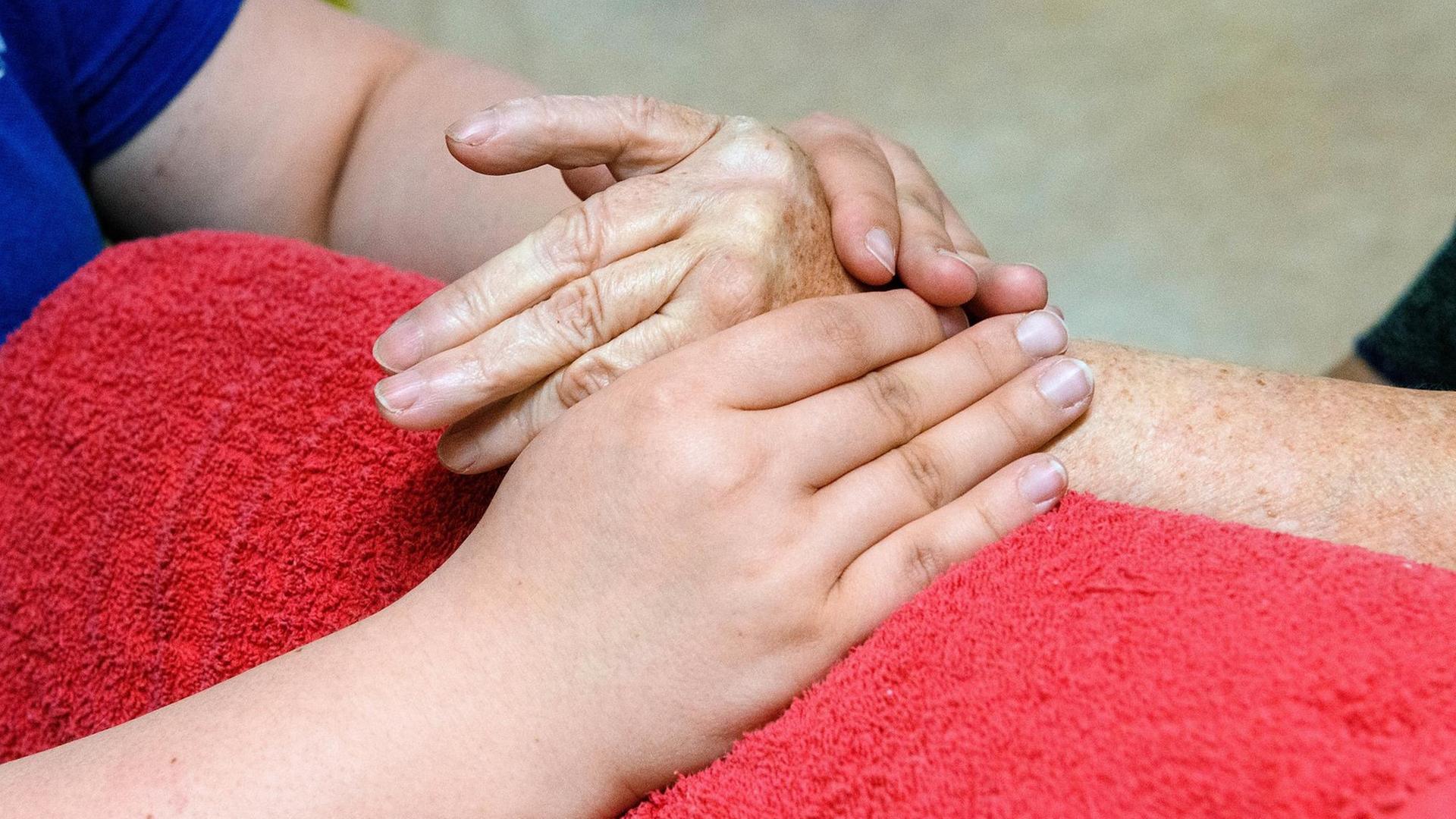 Hände einer an Arthritis erkrankten Patientin werden von einer Ergotherapeutin massiert. Die Massage der Hände wärmt und mobilisiert die entzuendeten Gelenke der Hand.