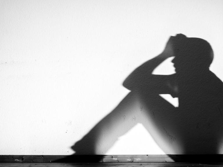 Der Schatten eines Mannes in verzweifelter Haltung wird an eine weiße Wand geworfen, aufgenommen am 01.02.2015 in Dresden (Sachsen)