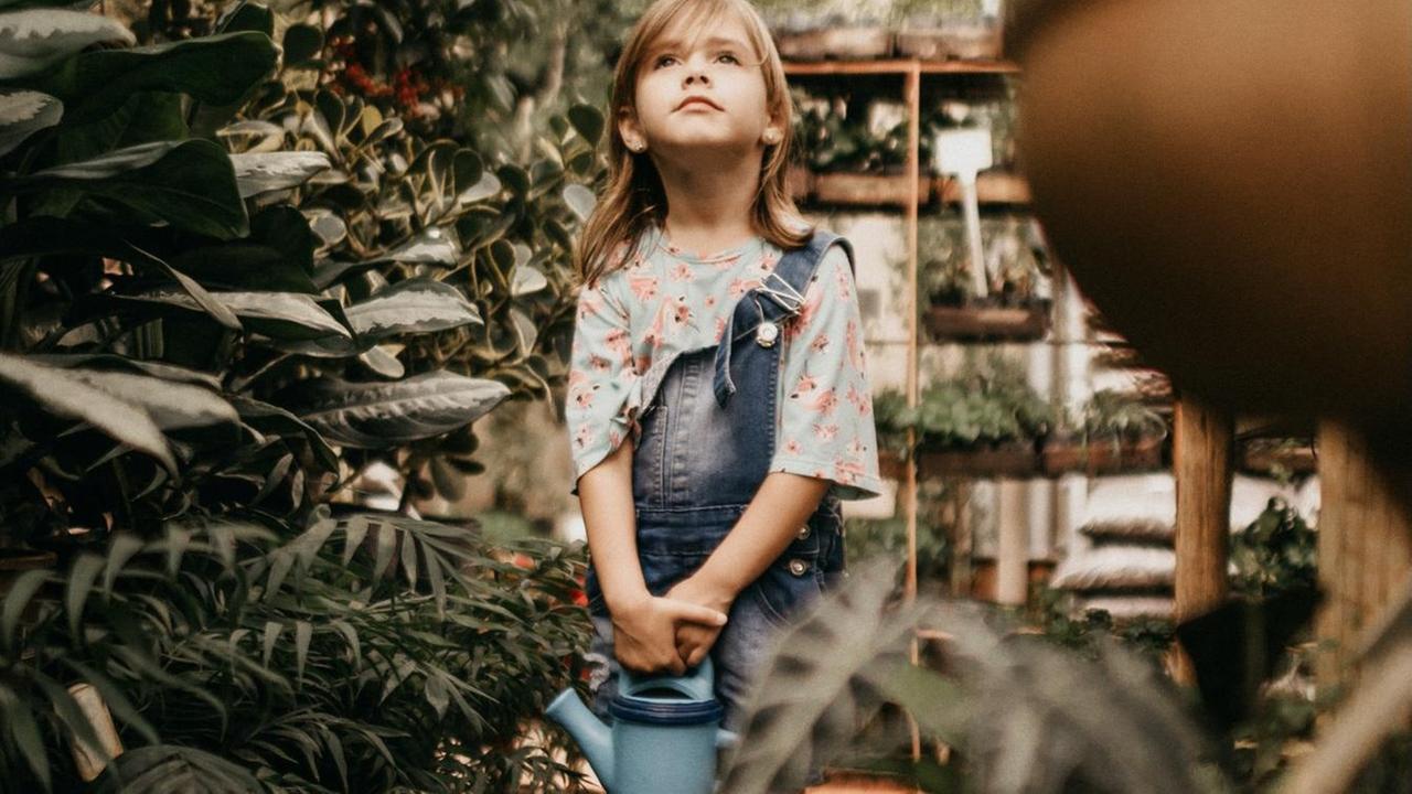 Ein Mädchen mit Latzhose und Gießkanne umringt von Pflanzen