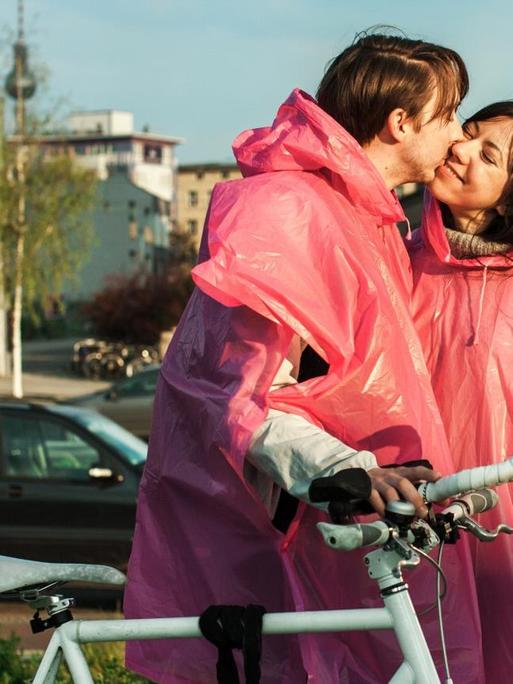 Ein Mann und eine Frau in den gleichen rosa Regenmänteln küssen sich auf der Straße.