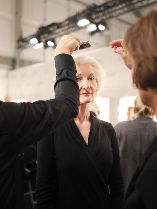 Während der Fashion Week in Berlin frisieren und schminken die Mitarbeiter einer Modenschau ein weibliches Modell, welches bereits im Rentenalter ist.