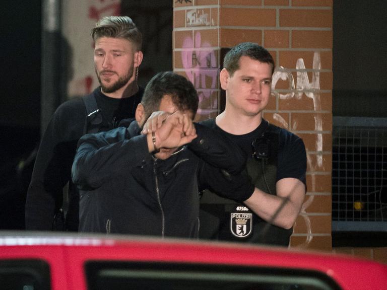 Polizisten führen bei einem Einsatz eine Person in Handschellen aus einem Haus in Berlin im Bezirk Neukölln.