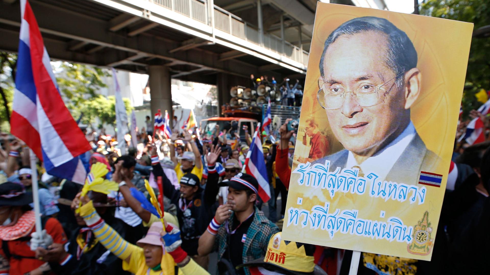 Demonstranten halten Plakate, die König Bhumibol zeigen
