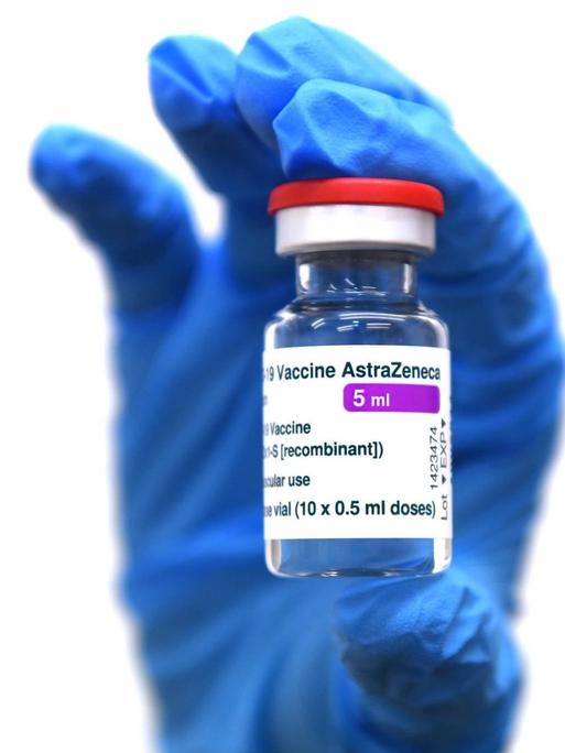 Eine Hand in blauem Schutzhandschuh hält ein Glasfläschchen mit dem Impfstoff von AstraZeneca im Lager des Universitätsklinikum in Tuebingen hohc.